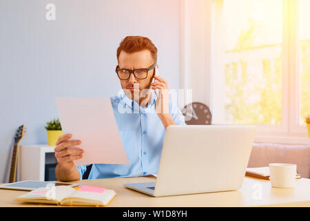 Zornigen Mann sprechen am Telefon von seinem Home Office, halten einige Papiere Stockfoto