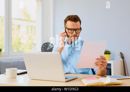 Zornigen mann Zahlen von Rechnungen und das Telefonieren mit Callcenter Stockfoto