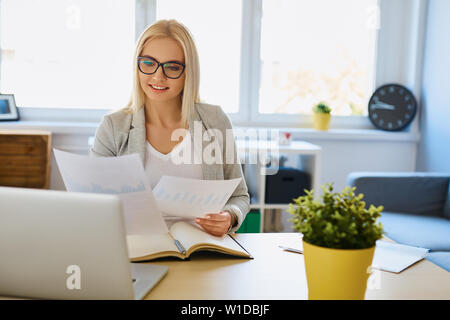 Schöne junge Frau arbeiten im Home Office mit Laptop und Dokumente Stockfoto