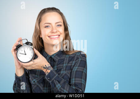 Junge Frau hält einen Wecker vor sich Stockfoto