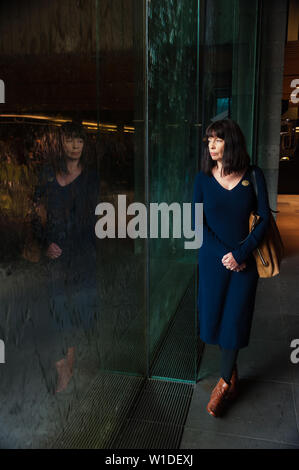 The Casual Observer - die Touristendammin und ihre Reflektion lehnen sich pensiver gegen eine große Glaswasserwand im Museum in Melbourne, Victoria. Stockfoto