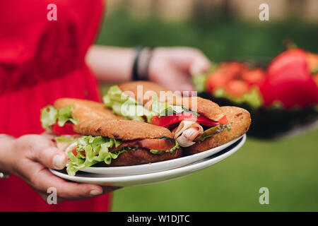 Frau bringt frische Sandwiches. Nahaufnahme der unkenntlich Frau, die köstliche hausgemachte Sandwiches auf Platten. Brot, Tomaten, Salat, Schweinefleisch. Stockfoto