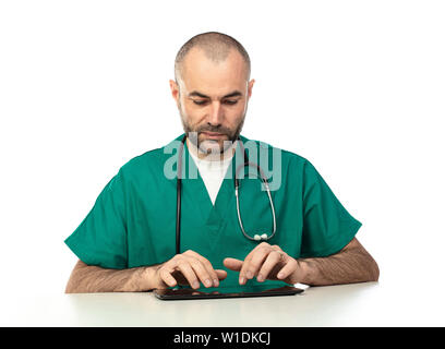 Arzt mit grüner Kleidung verwendet eine Tablette an einem Tisch sitzen. auf weißem isoliert. Technologie in der medizinischen Arbeit verwendet. Stockfoto