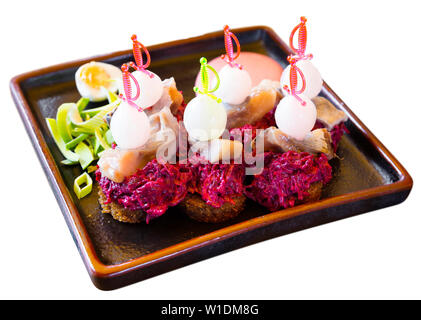 Kanapees von eingelegtem Hering, geriebene rote Rüben, Zwiebeln und Roggenbrot serviert mit Wachtelei und Soße. Analog der traditionellen russischen Salat Hering unter fu Stockfoto