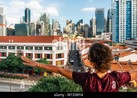 Chinatown, Singapur - Februar 8, 2019: Junge Frau steht zurück zu Kamera mit erhobenen Händen und genießt, Luftaufnahme von Chinatown mit roten Dächern Stockfoto