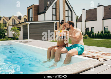 Schöne heteroseksual paar Sommer ausruhen. Der Mann und die Frau sitzen in der Nähe von Pool und mit frischen Cocktail Stockfoto