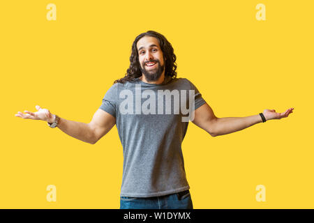 Ich weiß es nicht. Portrait des Denkens bärtiger junger Mann mit langen, lockigen Haar grau tshirt stehend mit erhobenen Armen und Kamera mit verwirrt Stockfoto