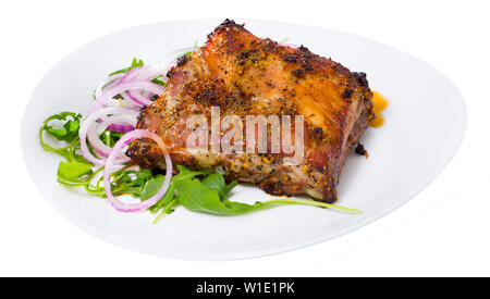 Saftigen Grill Rack von Schweinefleisch auf frischem Rucola mit Zwiebelringen serviert. Auf weissem Hintergrund Stockfoto