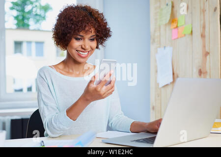 Glückliche junge Frau am Schreibtisch mit Ihrem Smartphone und Laptop Stockfoto