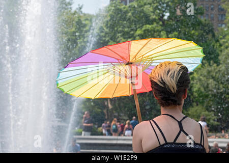 Eine Frau sitzt am Brunnen in den Washington Square Park mit einem Regenschirm, der LGBT-Regenbogen Farben. Am Tag der Trans Tag der Aktion Rallye. Stockfoto