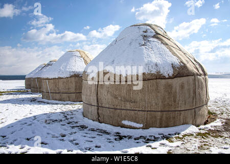 Jurten unter dem Schnee in der Mitte von einem schneebedeckten Feld gegen einen Himmel mit Wolken. Reisen Kirgisistan. Stockfoto