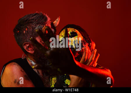 Halloween Mann mit satan Hörner Frau halten mit Totenkopf Make-up. Paar mit stop Geste auf rotem Hintergrund. Verbot, Ablehnung, Zurückweisung Konzept. Stockfoto