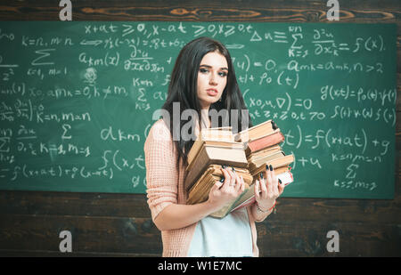 Sie liebt es zu lesen. Girl nerd hält schwere Stapel alter Bücher, schwarzes Brett Hintergrund. Mädchen Bücherwurm Bücher in der Bibliothek. Student ausgezeichnet gern lesen Stockfoto