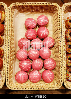 Süße Krapfen mit rosa Zuckerguss, Gebäck in Korb in Bäckerei, Ansicht von oben Stockfoto