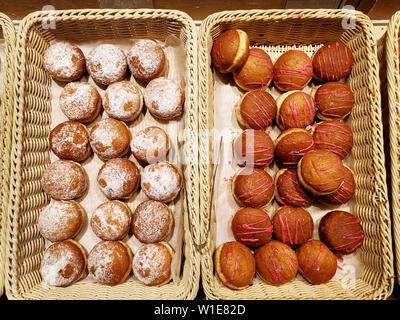 Verschiedene süße Krapfen, verglast und vereist und pulverisierte Gebäck in Körbe in Bäckerei Stockfoto