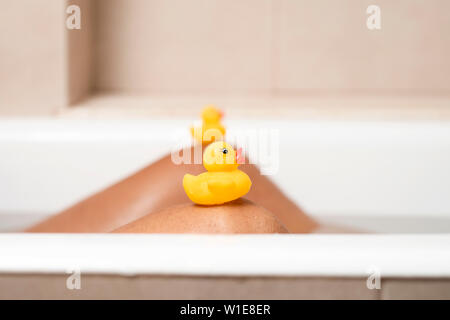 Nahaufnahme der Beine einer jungen kaukasischen Mann entspannen in der Badewanne eines Badezimmer, mit einigen Gummienten auf seinen Knien Stockfoto