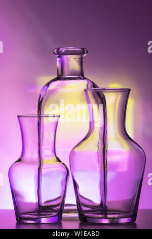 Glas transparent Geschirr - Flaschen verschiedener Größen, drei Stücke auf einem schönen bunten, Gelb, Lila und Rosa, Hintergrund. Sehr Stockfoto