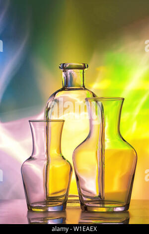 Glas transparent Geschirr - Flaschen verschiedener Größen, drei Stücke auf einem schönen bunten, Gelb, Blau und Rosa, Hintergrund. Sehr schöne Stockfoto