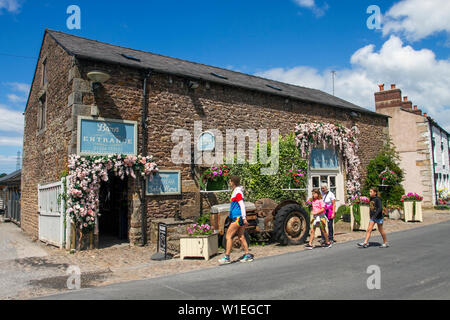 Ein steinernes Touristengeschäft am Straßenrand in Scorton, Lancaster. Vereinigtes Königreich Wetter Juli, 2019. Die Sonne bricht im ländlichen Lancashire über den floralen Darstellungen dekorierter Anwesen im ländlichen Dorf durch. Eine ehemalige Farm und historische Scheune am Straßenrand, die in ein Café & Restaurant umgewandelt wurde. Stockfoto