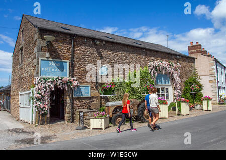 Ein steinernes Touristengeschäft am Straßenrand in Scorton, Lancaster. Vereinigtes Königreich Wetter Juli, 2019. Die Sonne bricht im ländlichen Lancashire über den floralen Darstellungen dekorierter Anwesen im ländlichen Dorf durch. Eine ehemalige Farm und historische Scheune am Straßenrand, die in ein Café & Restaurant umgewandelt wurde. Stockfoto