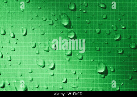 Große Tropfen von Wasser auf grün Textilien mit einem wasserdichten Effekt. Wasserabweisende Imprägnierung. Textur Tropfen auf das Gewebe. Stockfoto