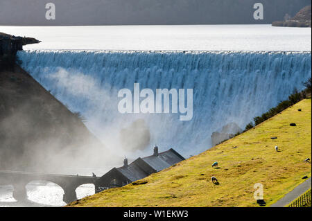 Die Besucher gehen über die Brücke wie Wasserkaskaden über Caban-coch Damm, bei Elan Valley Village in der Nähe von Rhayader in Powys, Wales, Vereinigtes Königreich, Europa Stockfoto