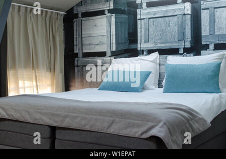 AMSTERDAM, NIEDERLANDE - Mai 2019: Gemütliches Bett mit grauen Bettdecken und Kissen in Blau ein Zimmer eines gemieteten Wohnung in Amsterdam. kleines Fenster platziert Stockfoto