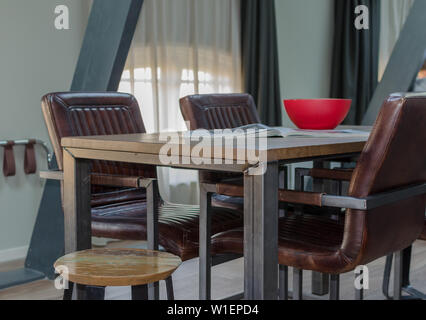 AMSTERDAM, NIEDERLANDE - Mai 2019: Holz und Metall Esstisch mit gemütlichen Ledersesseln, Holzboden in einem Mansardenzimmer mit einer gemieteten Wohnung. Stockfoto