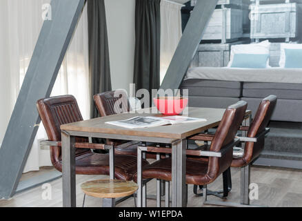 AMSTERDAM, NIEDERLANDE - Mai 2019: Holz und Metall Esstisch mit gemütlichen Ledersesseln, Holzboden in einem Mansardenzimmer mit einer gemieteten Wohnung. Stockfoto
