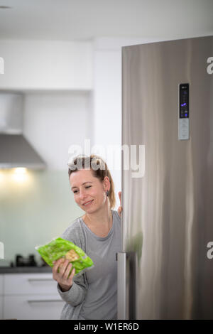 Hübsche, junge Frau, die Lebensmittel aus dem Kühlschrank nehmen, Kontrolle der Termine, gesunde Ernährung Konzept, Haushalt lifestyle Konzept Stockfoto