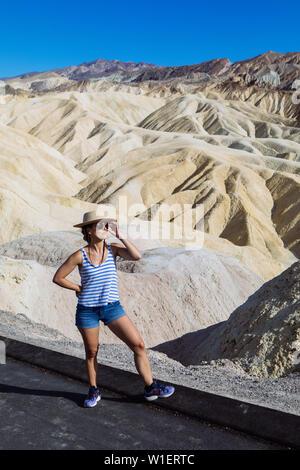 Tourist Woman posiert mit Hut und Schattierungen in Zabriskie Point, Furnace Creek, Death Valley National Park, Kalifornien, USA Stockfoto