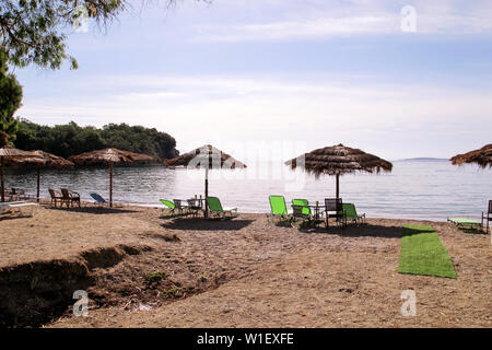 Lonely wicker Sonnenschirm am Strand mit Meerblick. Natürliche Bambus Sonnenschirme, Sommer Sonnenschirm Sonnenschirm, Liegestühle, Tisch, Solarium, Liegestühle und Sonnenschirme. Stockfoto