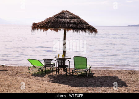 Lonely wicker Sonnenschirm am Strand mit Meerblick. Natürliche Bambus Sonnenschirme, Sommer Sonnenschirm Sonnenschirm, Liegestühle, Tisch, Solarium, Liegestühle und Sonnenschirme. Stockfoto