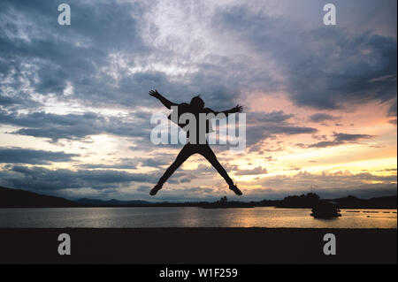 Silhouette glück Mann springen auf den See mit Sonnenuntergang Himmel Stockfoto
