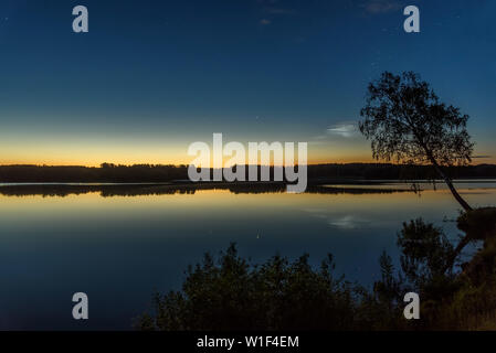 Tolle Nacht Landschaft mit silbrig leuchtende Wolken und Sterne im Himmel über den See und Baum und ihre Reflexionen im Wasser Stockfoto