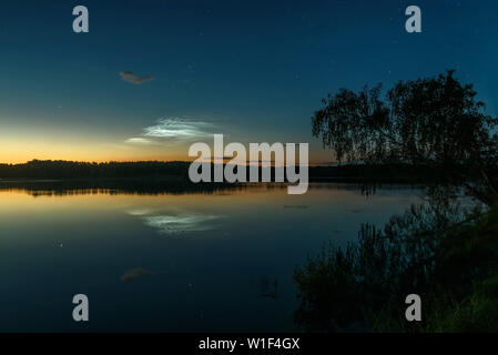 Tolle Nacht Landschaft mit silbrig leuchtende Wolken und Sterne im Himmel über den See und Baum und ihre Reflexionen im Wasser Stockfoto