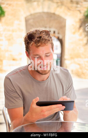 Mann mit Tablet 4g App im Sommer Cafe im Freien arbeiten. Junge kaukasier männlich Erwachsene schreiben auf Tablet oder lesen Reiseführer e online buchen während der Ferien. Stockfoto