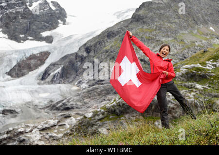 Schweiz Wanderer Wandern zujubeln, an denen Schweizer Fahne vor der Gletscher springen. Gerne asiatische Frau mit großen roten Flagge in der Natur. Stockfoto