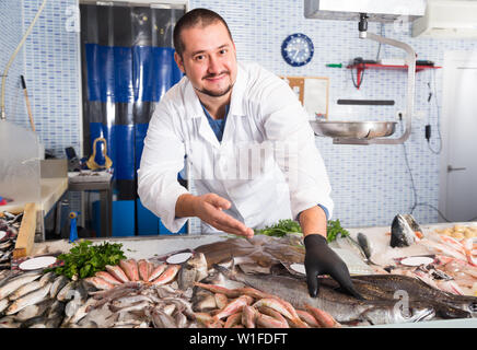 Verkäufer zeigt Hände Fisch auf Zähler im Supermarkt Stockfoto