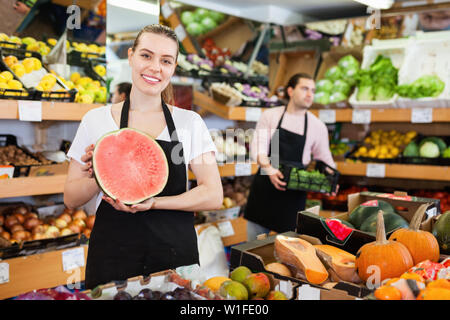 Junge gerne Fröhliche positive lächelnde Frau Verkäufer halten die Hälfte der Wassermelone in Händen Obst speichern Stockfoto