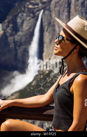 Touristenkaukasisch 30 Jahre Frauenprofil mit Hut und Schattierungen, die mit den Yosemite Falls im Glaciar Point Yosemite National Park, Kalifornien, USA posieren Stockfoto