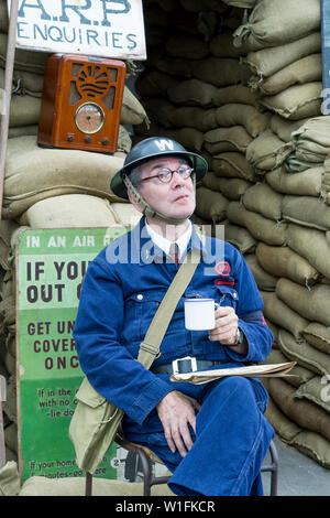 Kidderminster, Großbritannien. Juni 2019. Severn Valley Railways "die Rückkehr in die 1940er Jahre" beginnt dieses Wochenende mit einem fabelhaften Start in die Zeit, in der kostümierte Reenactors ihre Rolle spielen, um eine authentische Nachbildung des britischen Kriegsverbands zu bieten. Ein ARP (Air RAID Vorsorge) Aufseher sitzt im Dienst vor einem Luftschutzkeller, mit einem Cup, an einem alten Bahnhof entlang der Heritage Bahnlinie. Bild: Lee Hudson Stockfoto