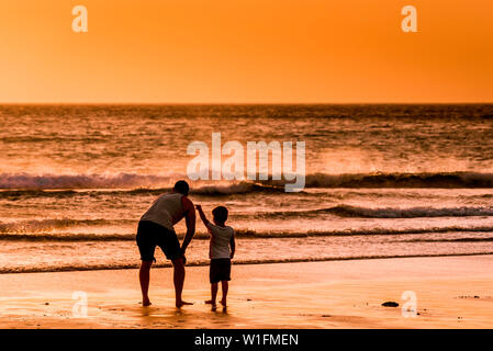 Ein Vater und sein Sohn genießen den wunderschönen Sonnenuntergang über den Fistral Beach in Newquay in Cornwall. Stockfoto