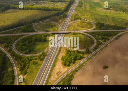 Kleeblatt interchange von oben gesehen. Drone Ansicht von Highway Kreuzung in der Landschaft mit Bäumen und Feldern. Stockfoto