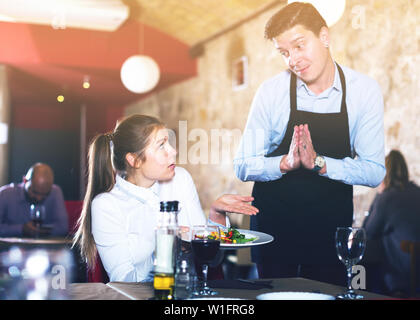 Weibliche client Unmut Ausdruck mit Essen sprechen zu entschuldigen, Kellner. Fokus auf Frau Stockfoto