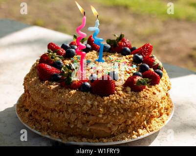 Party Food und festliche Konzept. Hausgemachten Kuchen zum Geburtstag mit Kerzen geschmückt, frische Heidelbeeren, Erdbeeren. Zwei Jahre alt. Stockfoto