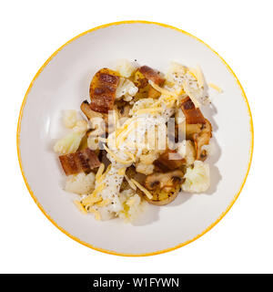 Blick von oben auf die gebackenen Kartoffeln mit Blumenkohl, Speck und Champignons mit Sauce und geriebenen Käse auf weiße Platte. Auf weissem Hintergrund Stockfoto