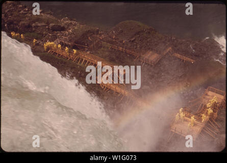 Blick NACH UNTEN AUF DIE HÖHLE DER WINDE, am Fuß der Klippen auf Goat Island zwischen den amerikanischen und kanadischen NIAGARA FALLS AUS DIESEM STADIUM, Besucher - geschützt durch gelbe wasserdichte Kleidung - EIN KOPF AUF DER ZENTRALEN ODER BRIDAL VEIL AMERICAN FALLS Stockfoto