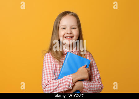 Portrait von ein wenig lustig Blonde Mädchen auf einem gelben Hintergrund. Ein Kind in einem rosa Hemd und Buch ist der Blick in die Kamera. Der Begriff der Bildung. Stockfoto