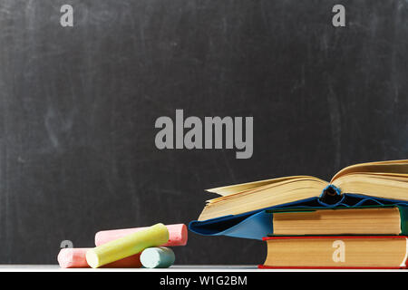 Einen Stapel Bücher und bunten Kreide auf dem Hintergrund der Tafel Schule. Der Begriff der Bildung. Zurück zu Schule. Kopieren Sie Platz. Stockfoto